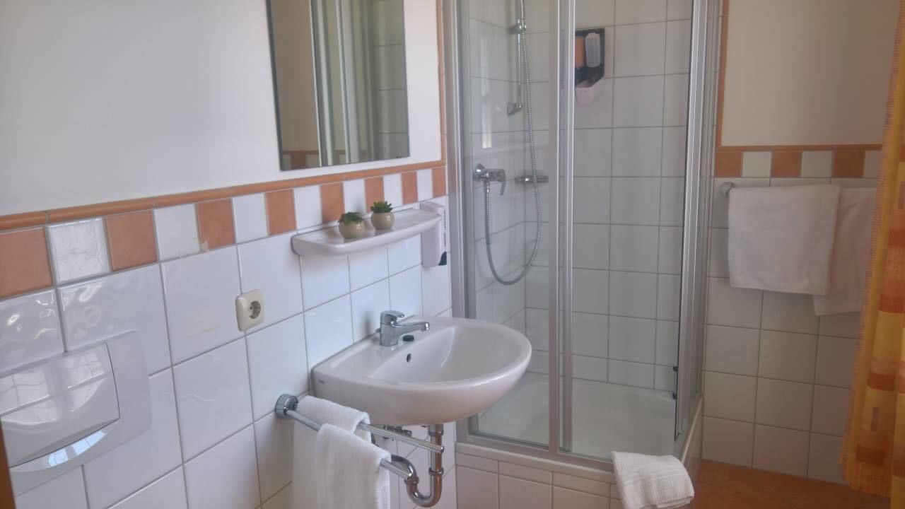 A bathroom with a sink, mirror, shower, and tiled walls.
