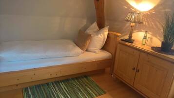 Una cama individual con almohadas, cabecera de madera, mesita de noche con lámpara, pequeño armario y alfombra verde a rayas.