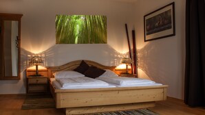A wooden bed with a headboard, two bedside tables with lamps, a large window with a bamboo forest view, and a framed picture on the wall. - Mettner Hof (Metten)