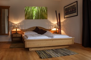 Uma cama de madeira com cabeceira, duas mesas de cabeceira com abajures, uma janela ampla com vista para uma floresta de bambu e um quadro na parede.