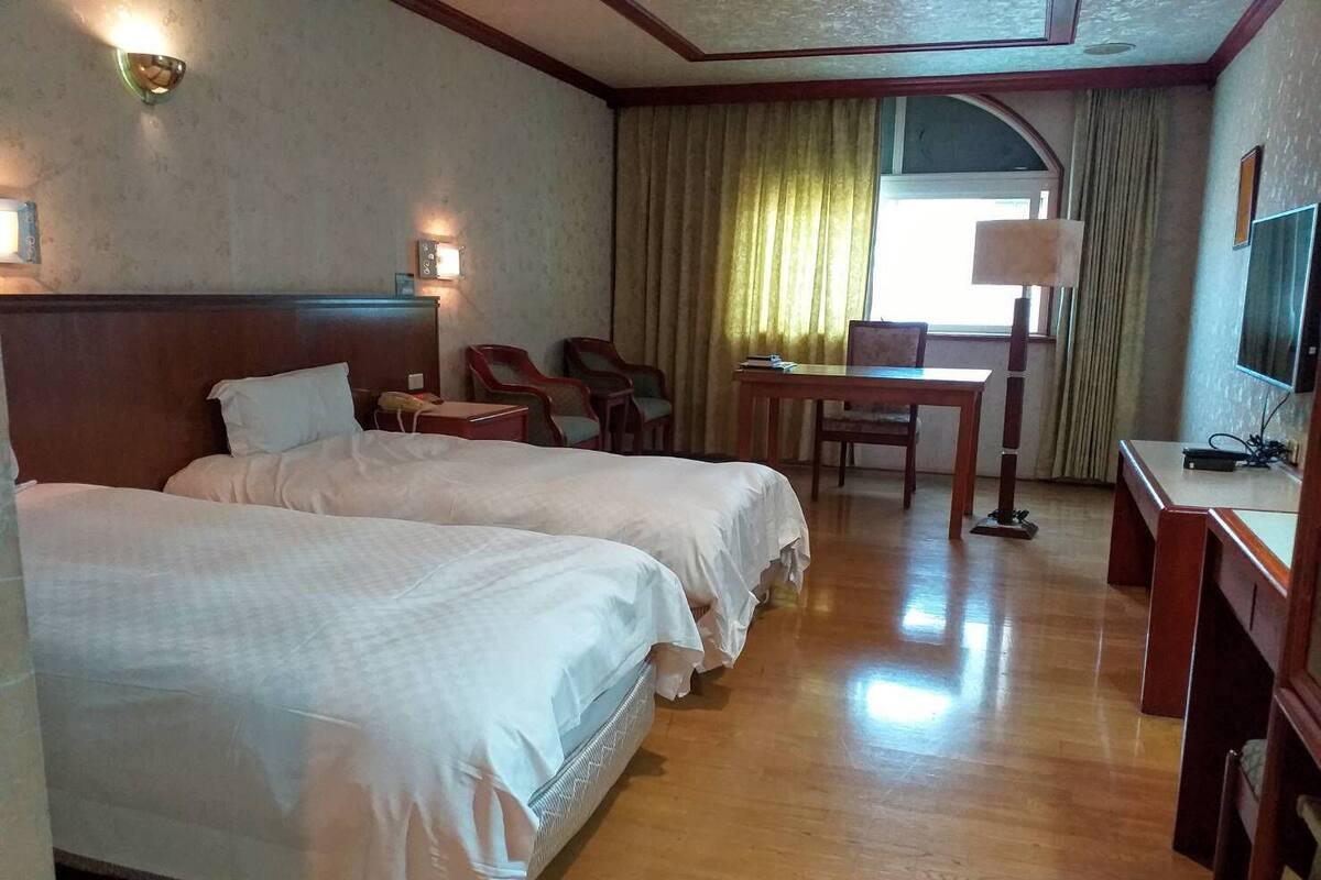 A hotel room with two beds, a desk, a chair, and a television.