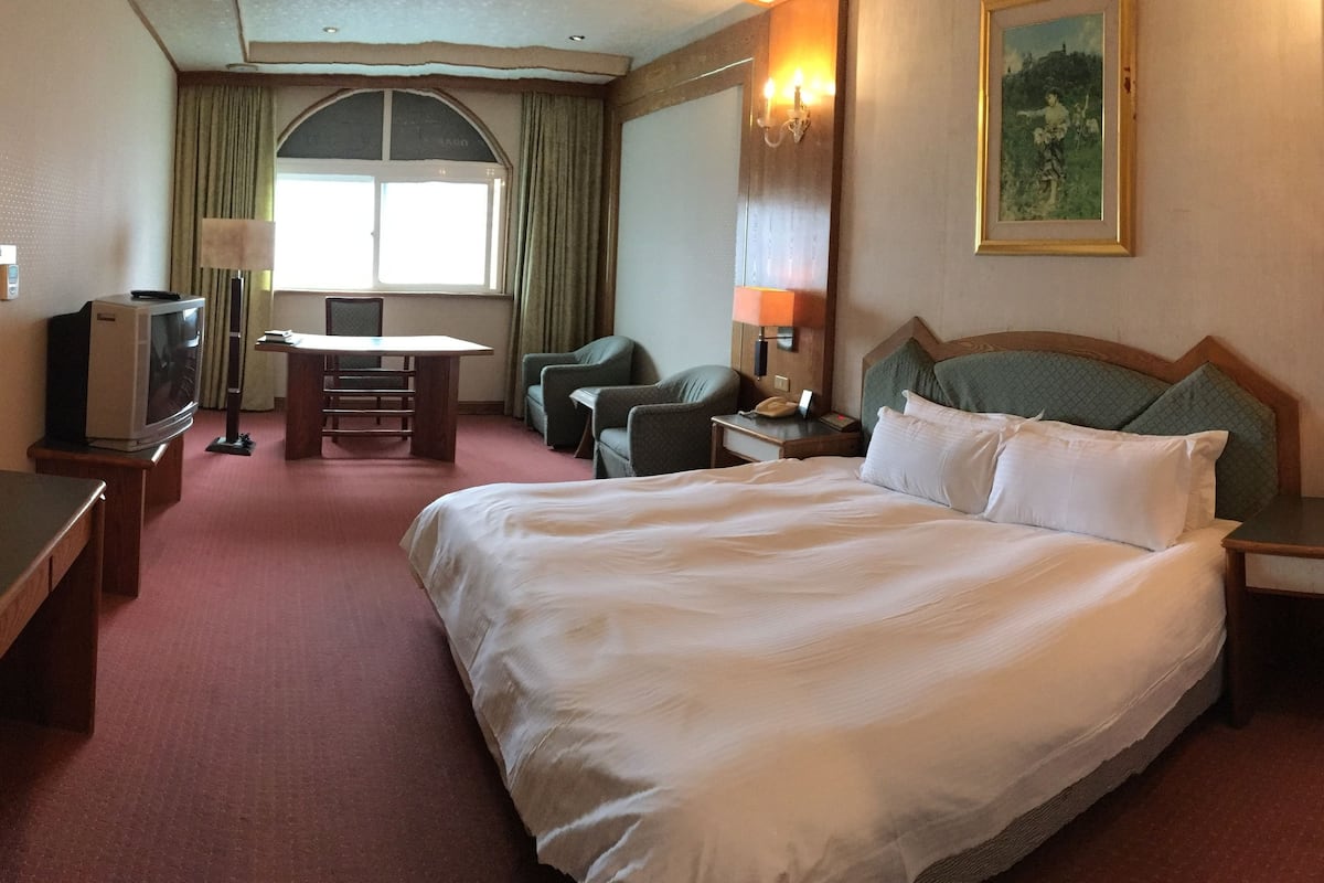 A hotel room with a large bed, a desk with a chair, a television, and a window with curtains.