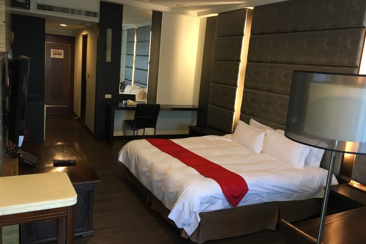 A hotel room with a large bed, a desk, a chair, a television, and a mirror.