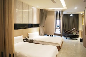 A hotel room with two beds, a minibar, a seating area with a sofa and table, and a view of the street through a window.