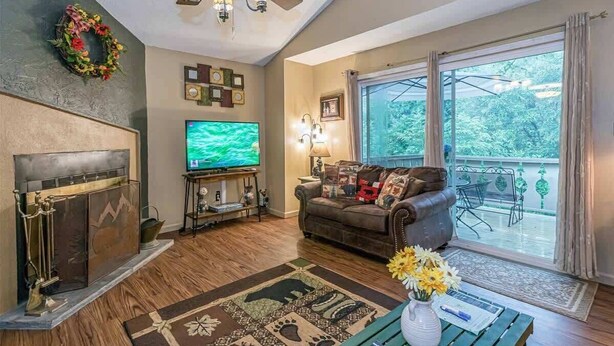 A living room with a fireplace, television, sofa, and a view of the outdoors.