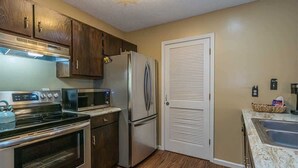 A kitchen with stainless steel appliances, wooden cabinets, a double door closet, and a marble countertop.