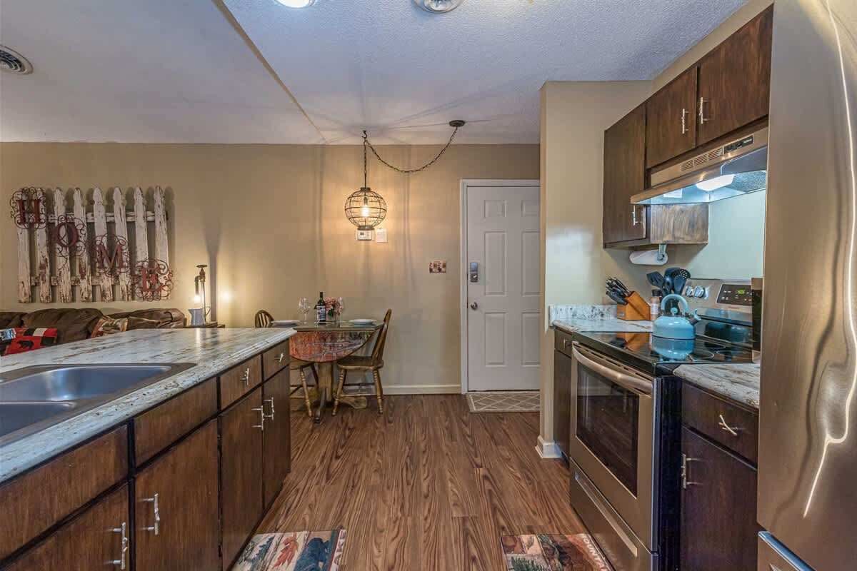 Une cuisine avec des meubles de rangement en bois, un plan de travail, une table à manger avec des chaises, un luminaire suspendu et une porte.