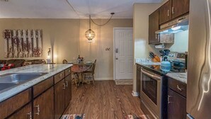 A kitchen with wooden cabinets, a countertop, a dining table with chairs, a hanging light fixture, and a door.
