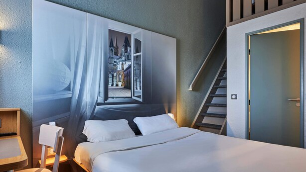A hotel room with a large bed, a desk, a chair, and a wall-mounted artwork depicting a castle.