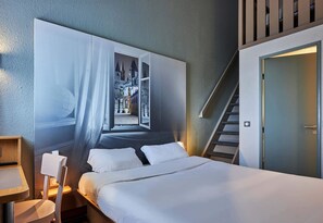 A hotel room with a large bed, a desk, a chair, and a wall-mounted artwork depicting a castle. - B&B HOTEL CAEN Sud (Ifs)