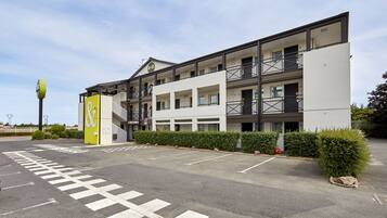 A multi-story hotel with a modern design, featuring balconies and a parking lot in front.