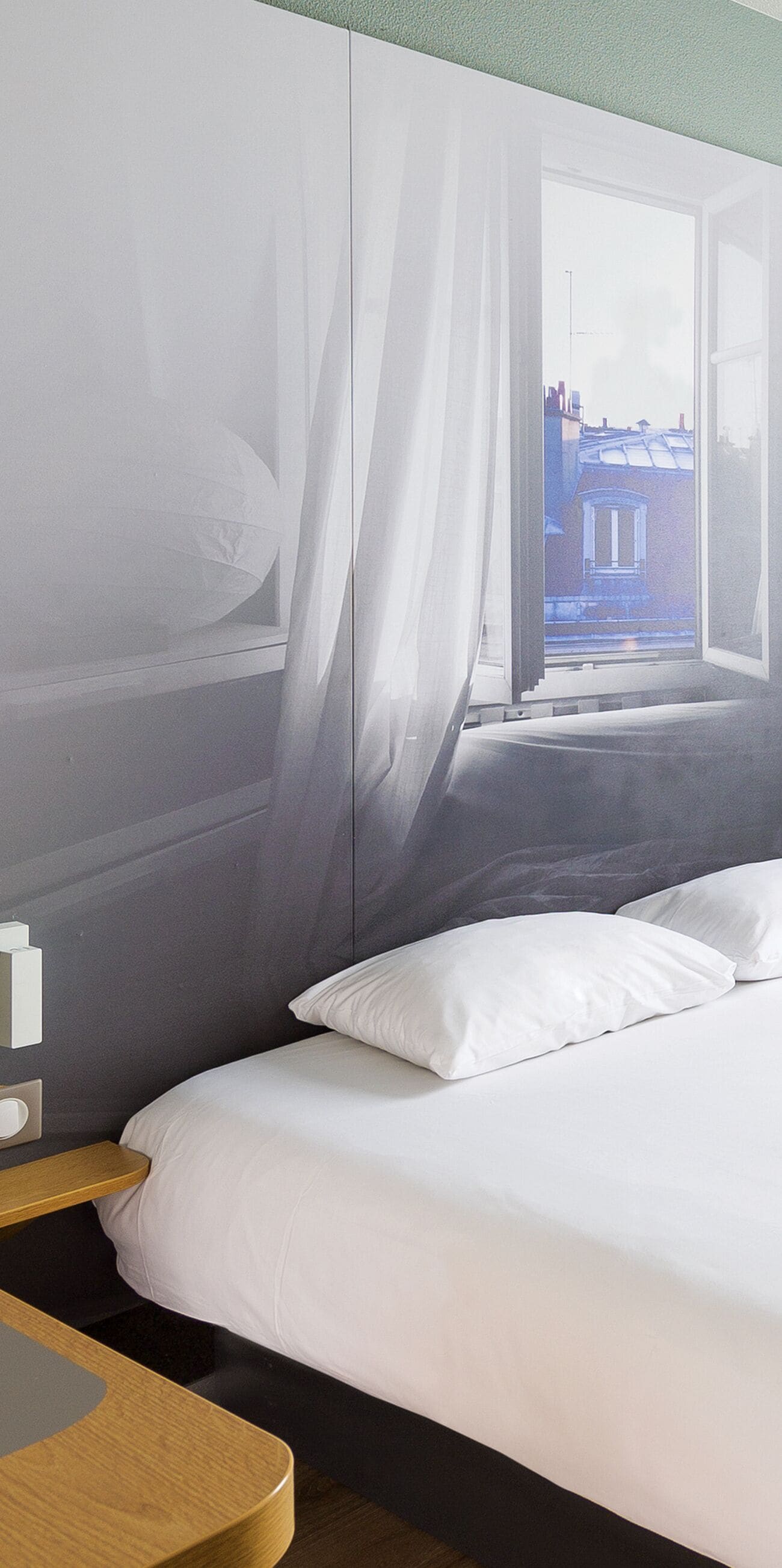 Una habitación de hotel con una cama, una mesita de noche y un ventanal con cortinas.