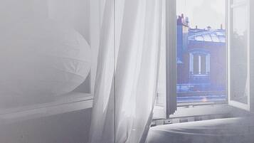 Una habitación de hotel con una cama, una mesita de noche y un ventanal con cortinas.