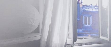 Una habitación de hotel con una cama, una mesita de noche y un ventanal con cortinas.