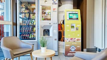 Et siddeområde med to stole og et lille bord, en automat og en drikkemaskine.