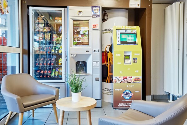 Una zona de estar con dos sillas y una mesita, una máquina expendedora y un dispensador de bebidas.