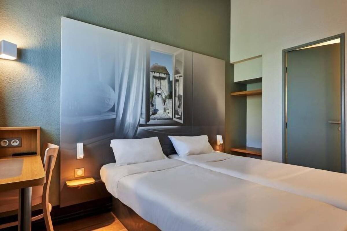 A hotel room with a bed, bedside tables, a desk, and a large painting on the wall.