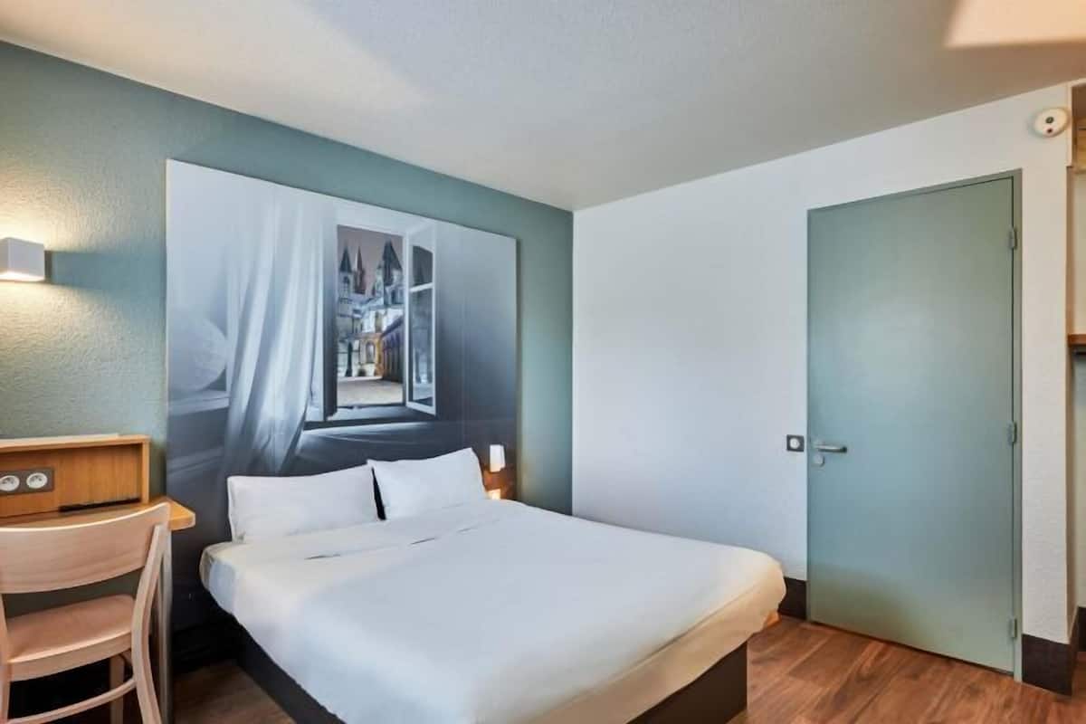 A hotel room with a bed, a desk, a chair, and a door.