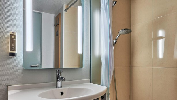Un baño con lavamanos blanco, espejo, ducha y toallero.