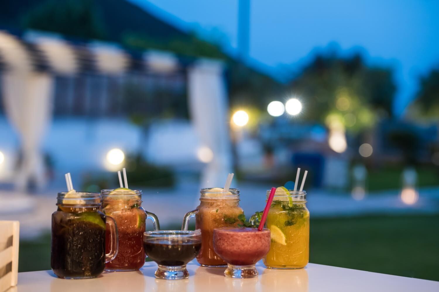 A variety of drinks on a table with a blurred outdoor background.