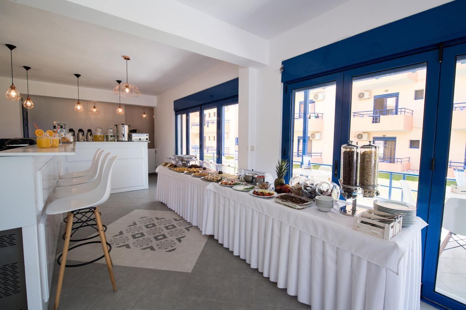 A modern kitchen with white cabinetry and a long breakfast bar, featuring a variety of breakfast items and a coffee station.