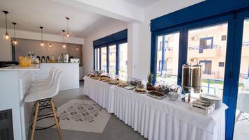 A modern kitchen with white cabinetry and a long breakfast bar, featuring a variety of breakfast items and a coffee station.