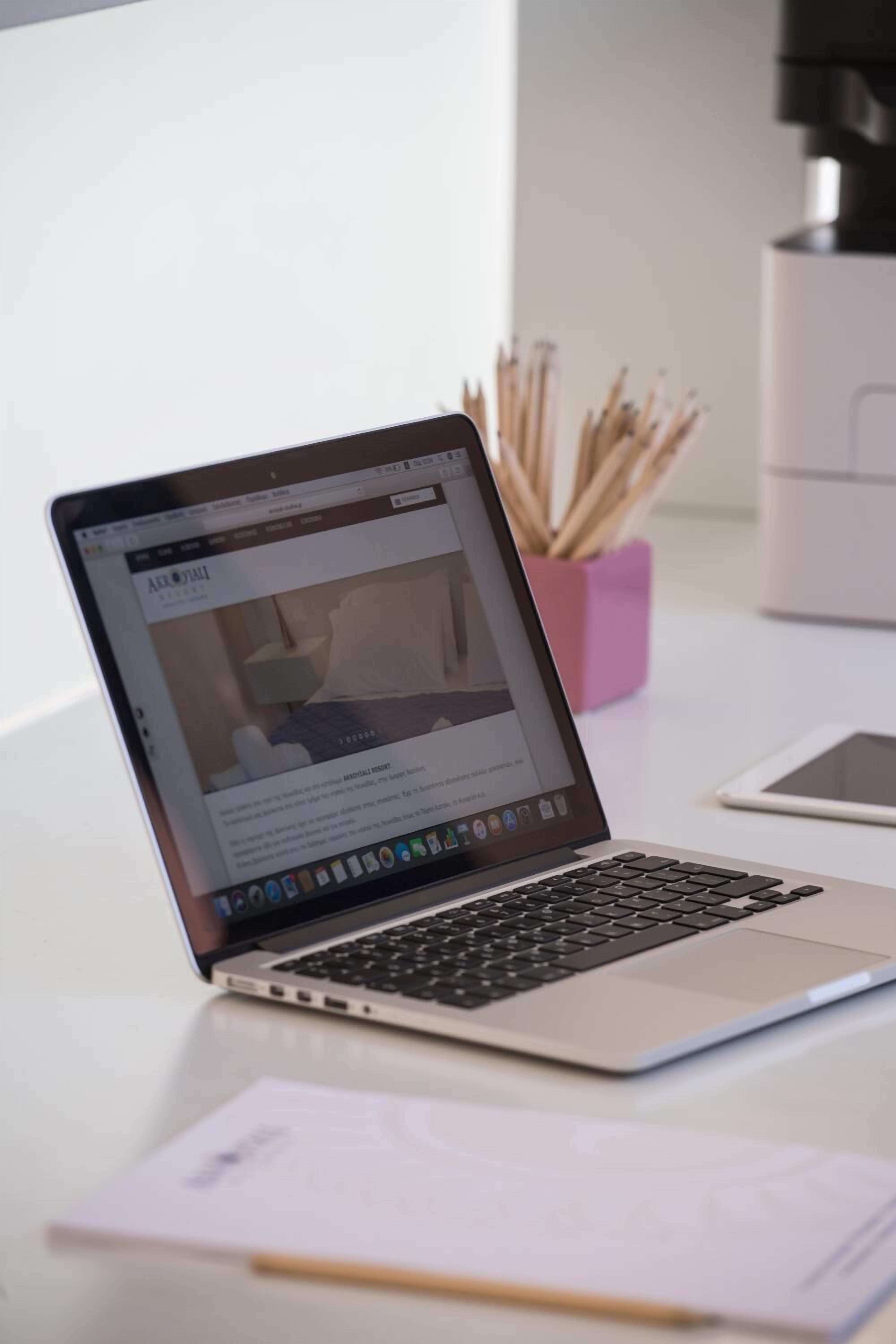 Ein Laptop auf einem Schreibtisch mit einem rosa Behälter, der Bleistifte, ein Tablet und einige Papiere enthält.