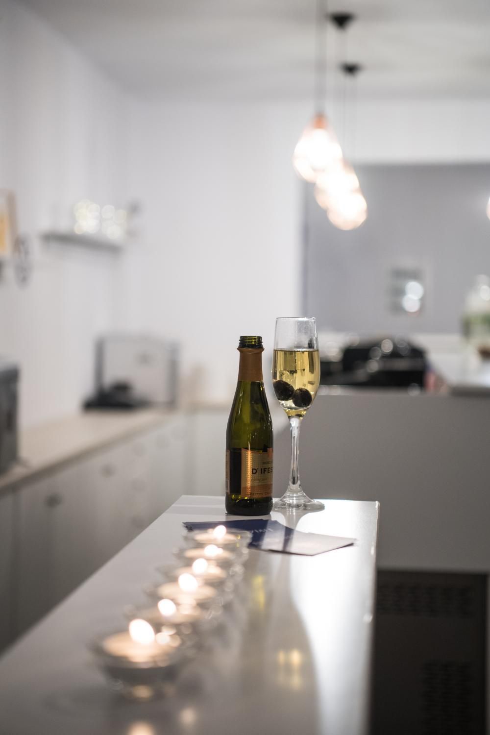 A bottle of wine and a glass on a reflective surface with a candle in the background.