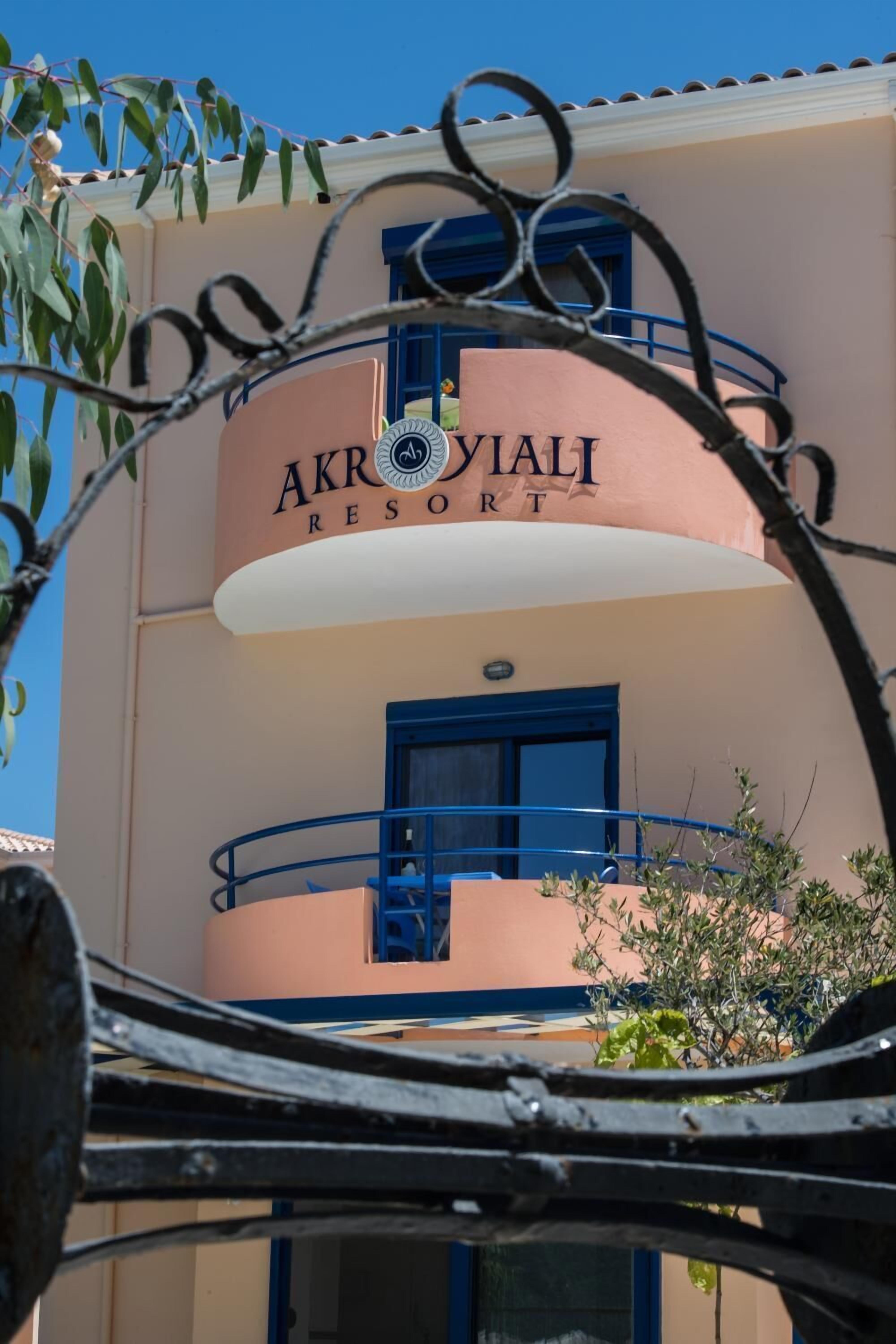 Das äußere Erscheinungsbild des Akroyali Resort mit einer auffälligen Beschilderung, einem Balkon mit blauen Geländern und einem strahlend blauen Himmel im Hintergrund.