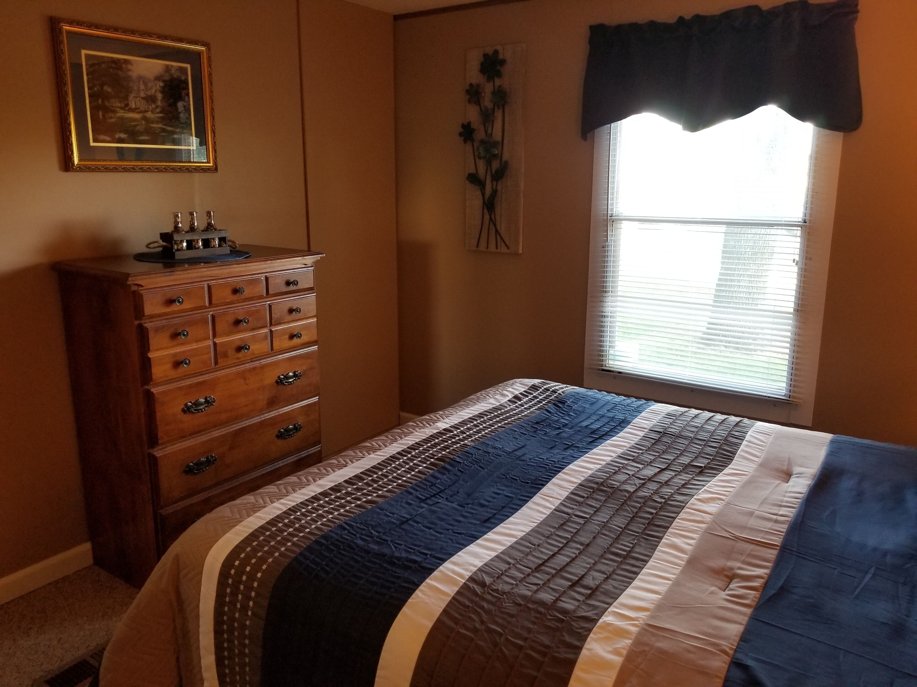 A bedroom with a bed, dresser, window, and wall decorations.