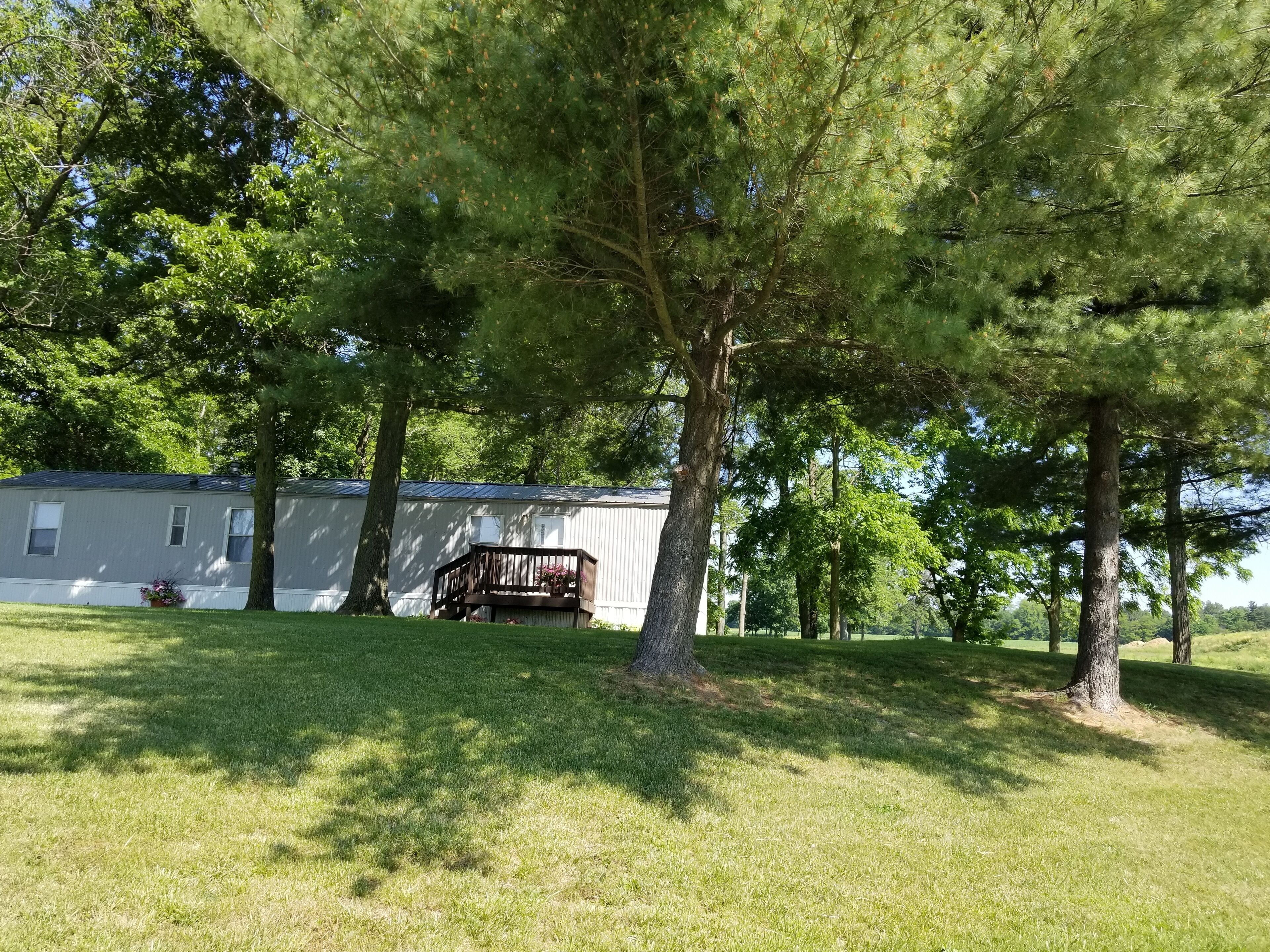 A residential area with a mobile home, a wooden deck, and surrounding trees.