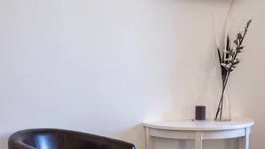 A corner of a room with a white table, a black leather chair, and a vase with branches. - B&B Civico 41 Salerno (Salerno)
