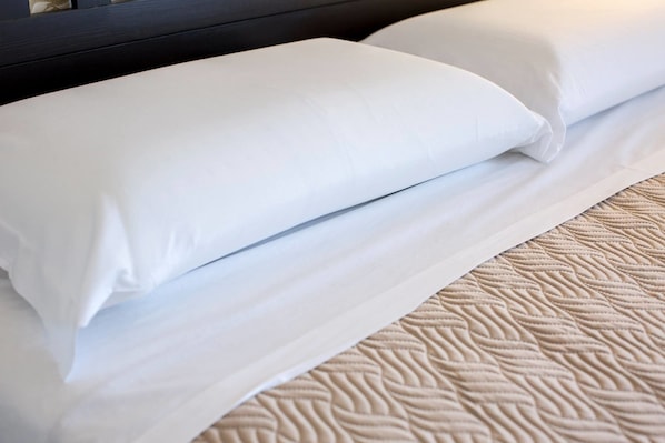 A neatly made bed with white linens and a textured beige bedspread.