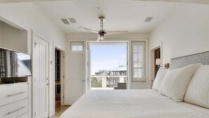 Un dormitorio con una cama, ventilador de techo, televisor y vistas al exterior.