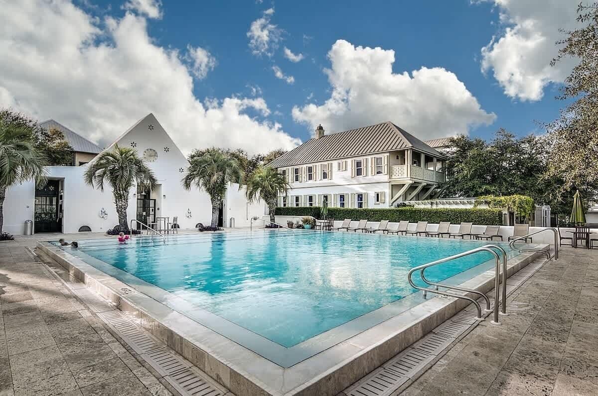A swimming pool with a white building in the background, palm trees, and a clear sky.
