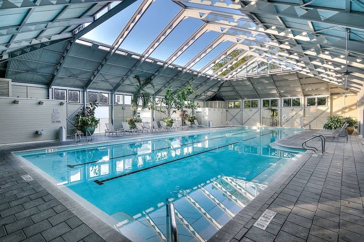 An indoor swimming pool with a glass ceiling, surrounded by lounge chairs and potted plants.