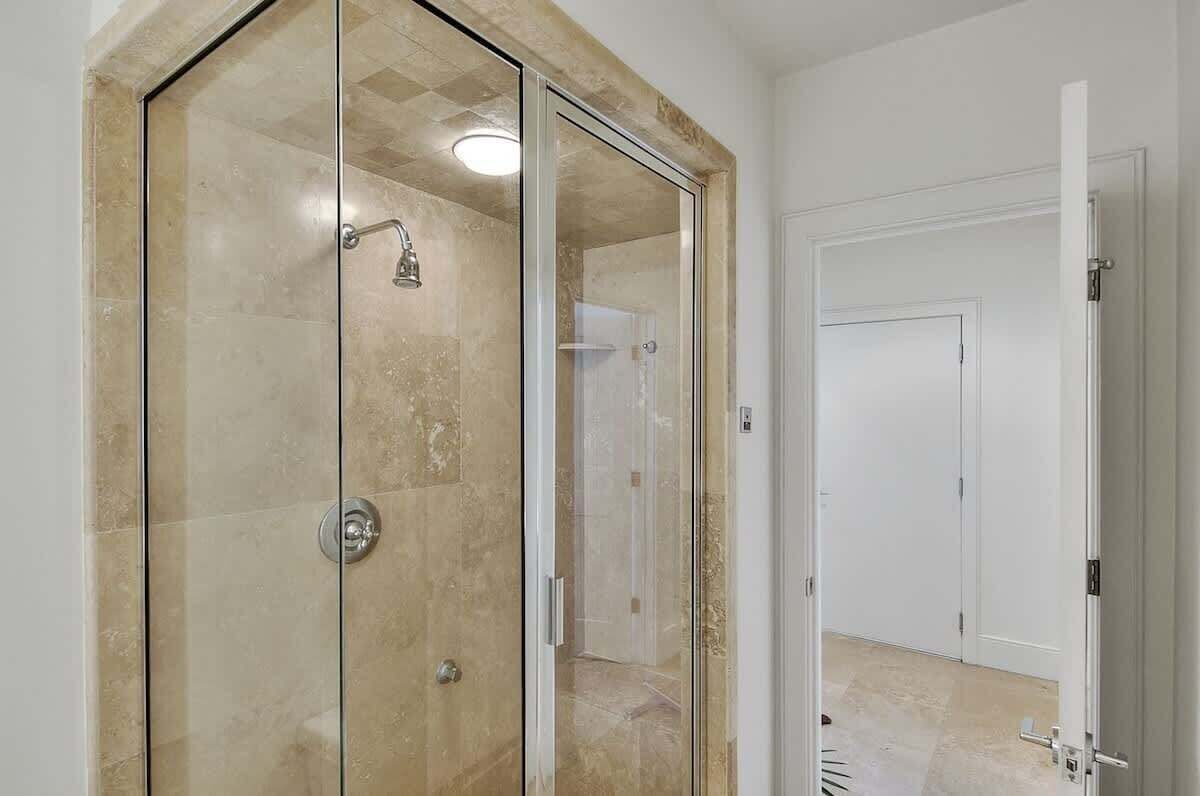 A bathroom with a glass-enclosed shower, a white door, and a tiled floor.