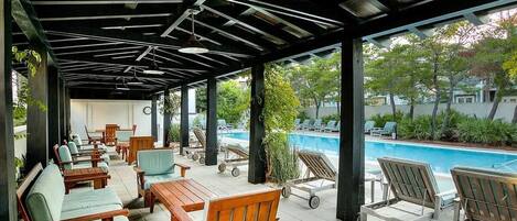 A covered outdoor seating area with wooden furniture and a view of a swimming pool.