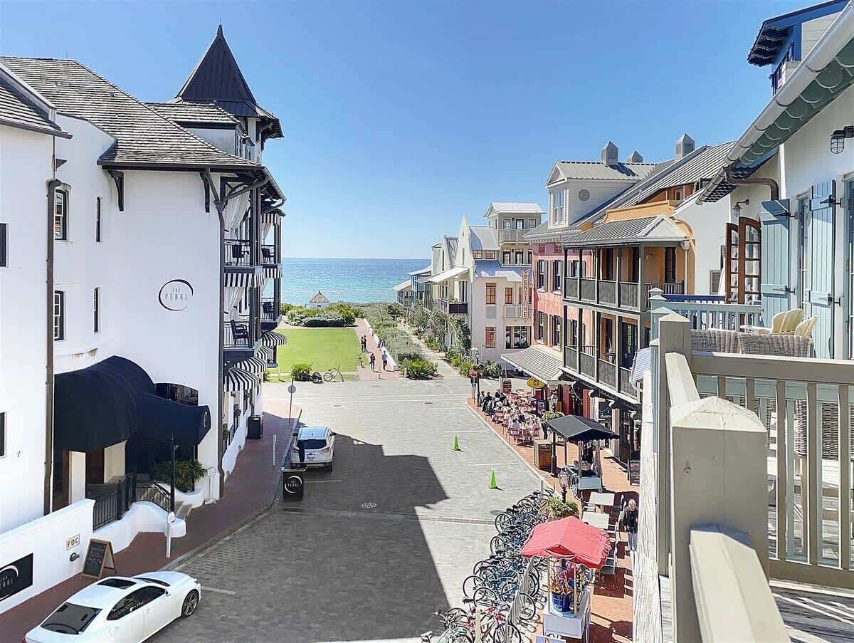 Una calle costera con edificios, un coche aparcado y vistas al mar.