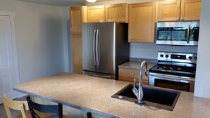 A kitchen with wooden cabinets, a stainless steel refrigerator, an oven, and a granite countertop. - Lime Ridge Guest House  (Elkhart Lake)