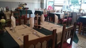 Un restaurant avec de nombreuses tables dressées pour le service, doté de chaises en bois et de nappes vertes.