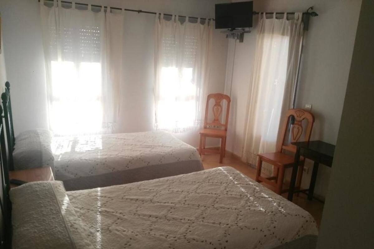A room with two beds, a television mounted on the wall, and a chair.