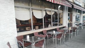 Un café en plein air avec des tables et des chaises, un mur en briques et un auvent à rayures.