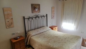Une chambre à coucher comprenant un lit, une table de chevet, une commode et des œuvres d’art accrochées aux murs.