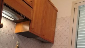 Ett kompakt kök med träskåp, en diskho i rostfritt stål och ett fönster med persienner.