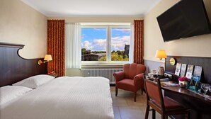A hotel room with a large bed, a desk with a chair, a TV, and a window with curtains. - Altes Gasthaus Kuhr (Papenburg)
