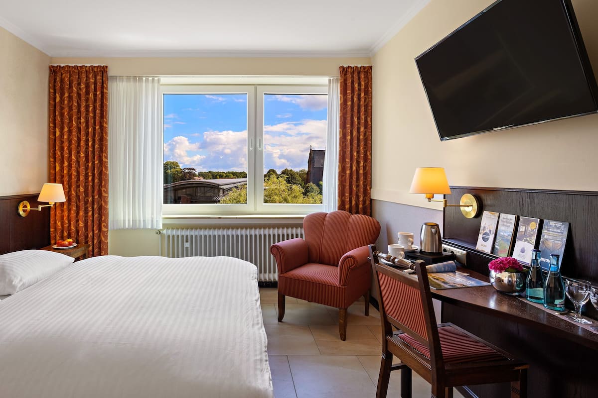 A hotel room with a large bed, a desk with a chair, a TV, and a window with curtains.