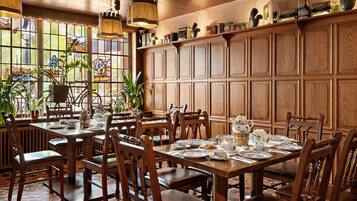 Un comedor con mesas y sillas de madera, ventanas de vitral y una variedad de vajilla.