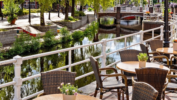 A riverside café with wicker tables and chairs, a bridge in the background, and a canal. - Altes Gasthaus Kuhr (Papenburg)