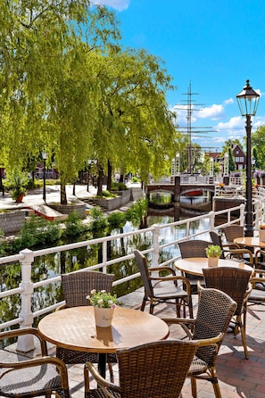 A riverside café with wicker tables and chairs, a bridge in the background, and a canal. - Altes Gasthaus Kuhr (Papenburg)